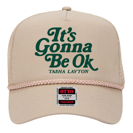 A beige hat with the text 'It's Gonna Be Ok' and the name 'TASHA LAYTON' on it, featuring a green and black color scheme.